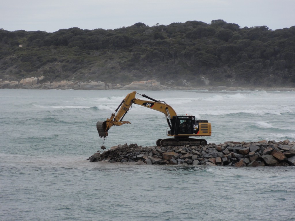 Excavator levelling the stone in place forming the wall